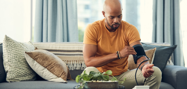 Shot of a young man taking his blood pressure while sitting on the sofa at home