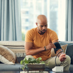 Shot of a young man taking his blood pressure while sitting on the sofa at home