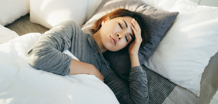 Young Asian woman with hand on forehead lying in bed and feeling sick