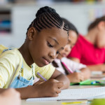 Cute pupil writing at desk in classroom