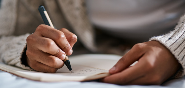 Cropped shot of a man writing in a notebook on his bed at home