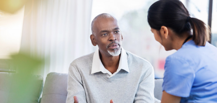 Serious senior African American man gestures while asking a female healthcare professional a question about his diagnosis.