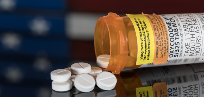 Prescription bottle for Oxycodone tablets and pills on wooden table with USA flag in background