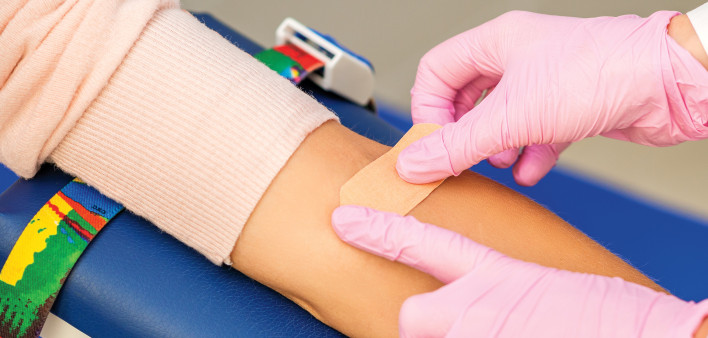 pink gloves putting band aid on arm after blood draw