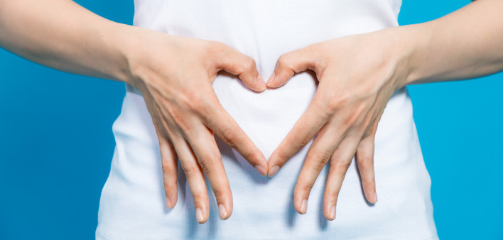 Young woman who makes a heart shape by hands on her stomach