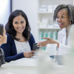 Smiling pharmacist talks withe young boy and his mom about his medication. The boy's mom is holding a smartphone.