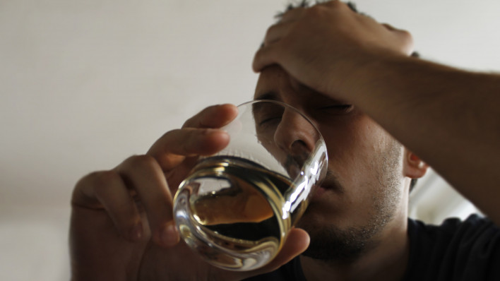 Drunk young adult male holding glass of alcohol, studio shot.