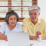 Asian couple seniors use laptop video conference with doctor about illness and prescription pill in living room at home