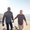 gay couple walking and in hand on the beach smiling