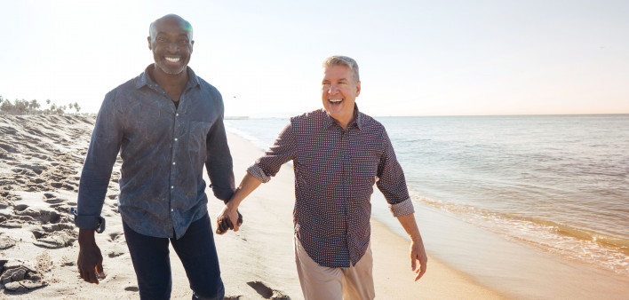 gay couple walking and in hand on the beach smiling