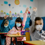 Elementary schoolchildren wearing a protective face masks in the classroom. Education during epidemic.