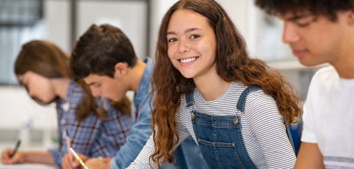 Satisfied young woman looking at camera while her friends studying at college. Team of multiethnic students preparing for university exam.