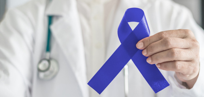 Dark blue ribbon for colon - colorectal cancer awareness on medical doctor's hand