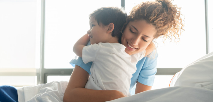 Beautiful sweet little boy hospitalized in the pediatrics ward hugging young nurse both smiling