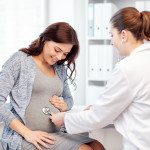 pregnancy, gynecology, medicine, health care and people concept - gynecologist doctor with stethoscope listening to pregnant woman baby heartbeat