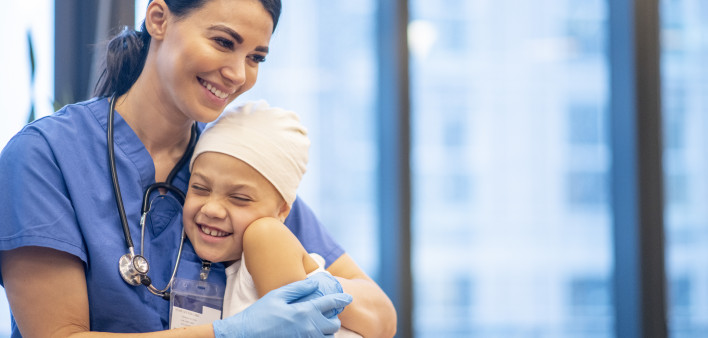 Nurse Hugging Young Cancer Patient stock photo A young Latin female nurse hugs her cancer patient as they enjoy a brief moment together. The young girl is smiling and happy. The nurse is wearing blue scrubs with a stethoscope around her neck, while the yo