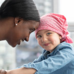 A cute elementary age girl with cancer is wearing a pink scarf on her head.