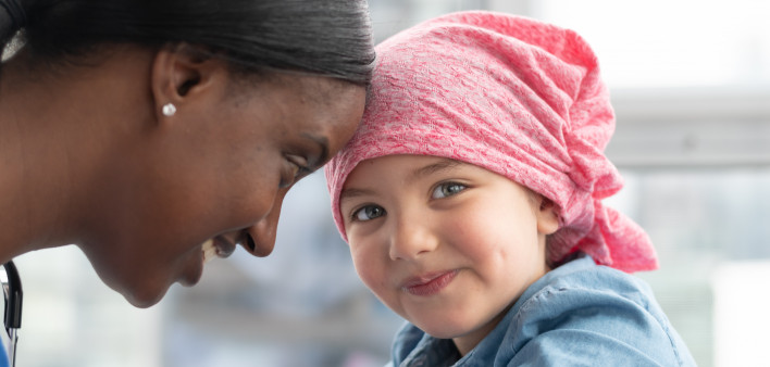 A cute elementary age girl with cancer is wearing a pink scarf on her head.