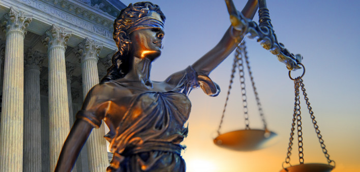 A statue of the blindfolded lady justice in front of the United States Supreme Court building as the sun rises in the distance symbolizing the dawning of a new era.
