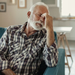 A Distraught Senior Man Suffering From a Migraine While Sitting on the sofa in the Living Room