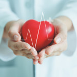Female medical doctor holding red heart shape in hand with graphic of heart beat, cardiology and insurance concept