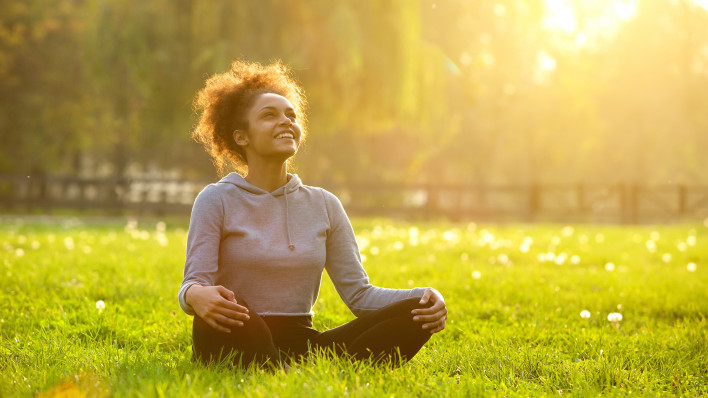 Happy young woman sitting outdoors in yoga position