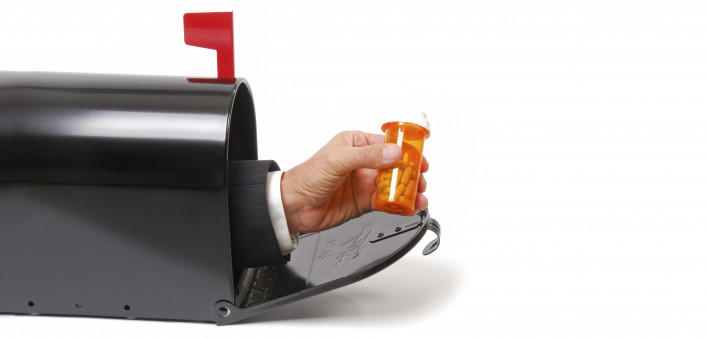 a hand holding a prescription coming out of a mailbox