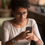 Upset confused african woman holding cellphone having problem with mobile phone,