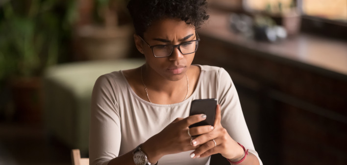 Upset confused african woman holding cellphone having problem with mobile phone,