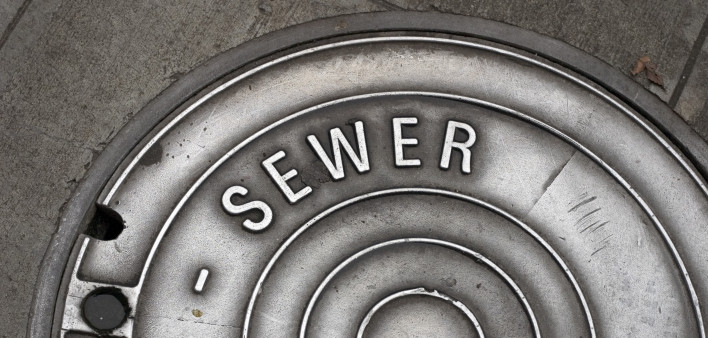 A sewer manhole cover in the sidewalk that is well worn and shiny
