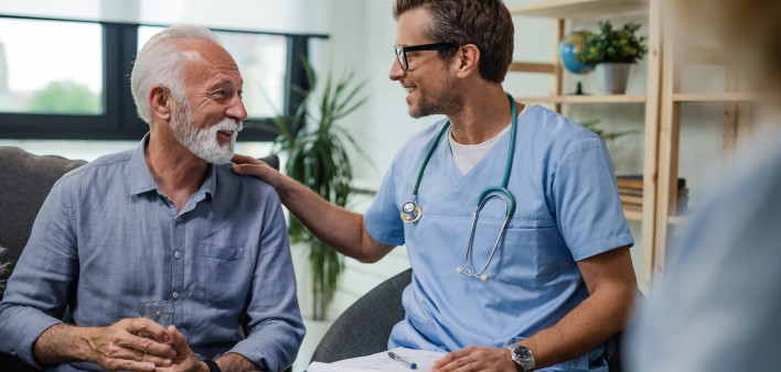 Happy doctor talking to senior male patient while being in a home visit.