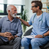 Happy doctor talking to senior male patient while being in a home visit.