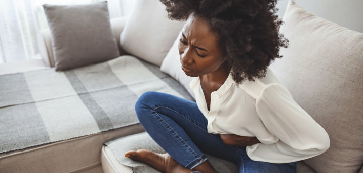 woman lying on her sofa alone and suffering from period cramps