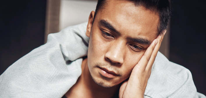 sick man covered in blankets holding his head and holding a cup