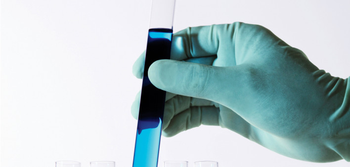 gloved hand holding test tubes with color liquid