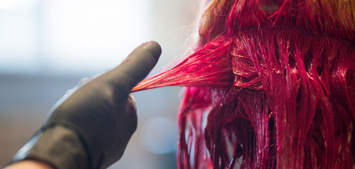 Young woman getting her hair dyed a vivid red in salon