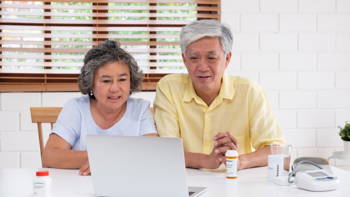Asian couple seniors use laptop video conference with doctor about illness and prescription pill in living room at home