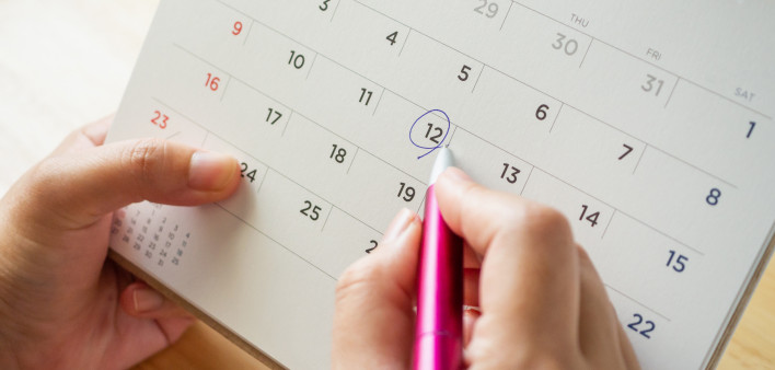 Calendar page with female hand holding pen on desk table
