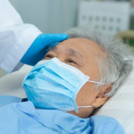 Doctor touching and checking Asian senior or elderly old lady woman patient wearing a face mask in hospital for protect infection and kill Novel Coronavirus Covid-19 virus
