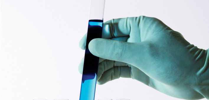 gloved hand holding test tubes with color liquid