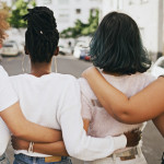 Rearview shot of a group of unrecognizable young friends walking with their arms around each other in the city