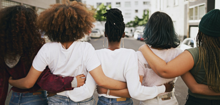 Rearview shot of a group of unrecognizable young friends walking with their arms around each other in the city