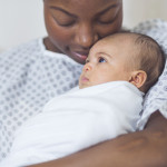 Beautiful African American mother in a hospital gown holds her newborn baby