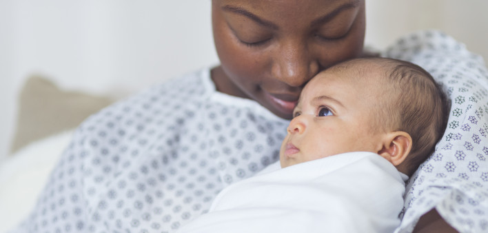 Beautiful African American mother in a hospital gown holds her newborn baby
