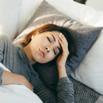 Young Asian woman with hand on forehead lying in bed and feeling sick