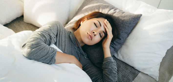 Young Asian woman with hand on forehead lying in bed and feeling sick