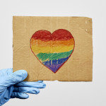 LGBTQ friendly healthcare system worker holding handmade placard with heart-shaped rainbow flag.