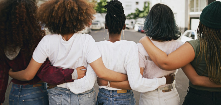 Rearview shot of a group of unrecognizable young friends walking with their arms around each other in the city