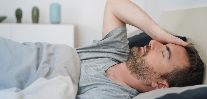 sick man lying down in bed and holding head