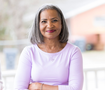 Beautiful African American senior woman stands confidently on her front porch. She is smiling at the camera.